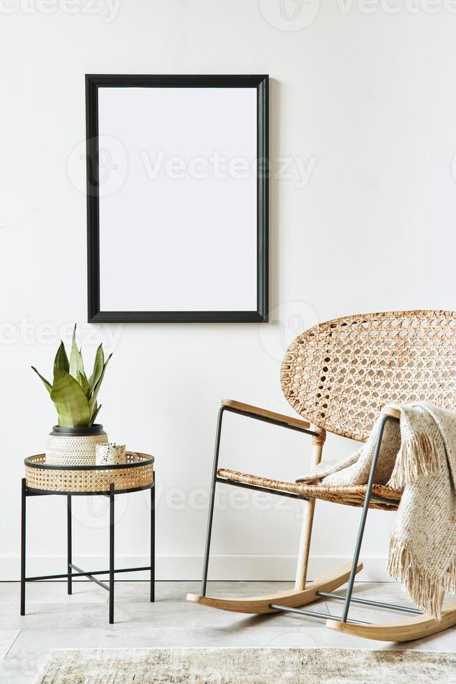 Retro modern compositon of living room interior with design rattan armchair, black mock up poster frame, coffee table, plant, decoration, white wall and personal accessories. Template. photo