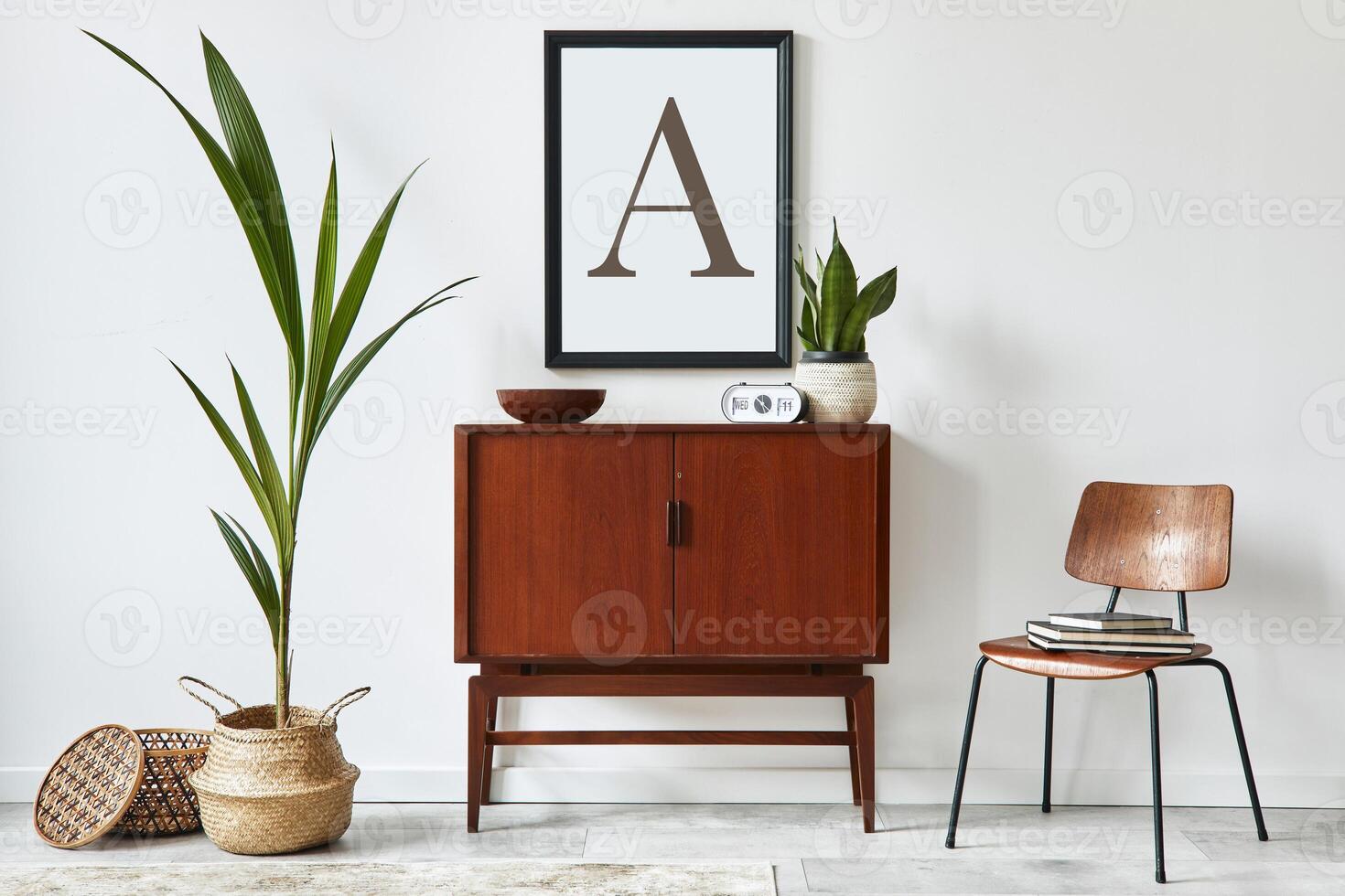 Stylish interior design of living room with wooden retro commode, chair, tropical plant in rattan basket, decoration and elegant personal accessories. Mock up poster frame on the white wall. Template. photo