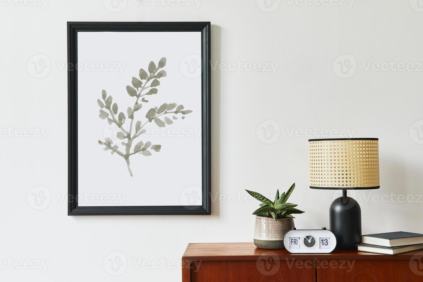 Retro modern compositon of living room interior with design teak commode, black mock up poster frame, clock, plant, decoration, white wall and personal accessories. Template. photo