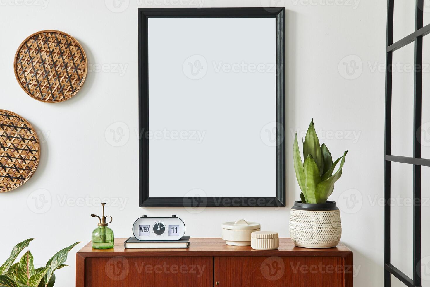 Retro modern compositon of living room interior with design teak commode, black mock up poster frame, clock, plant, decoration, white wall and personal accessories. Template. photo