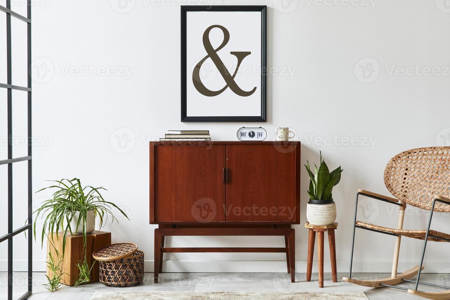 Stylish interior design of living room with wooden retro commode, chair, plant, rattan decoration, cube and elegant personal accessories. Mock up poster frame on the white wall. Template. photo