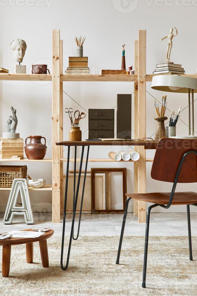 Unique artist workspace interior with stylish desk, wooden easel, bookcase, artworks, painting accessories, decoration and elegant personal stuff. Modern work room for artist. Template. photo