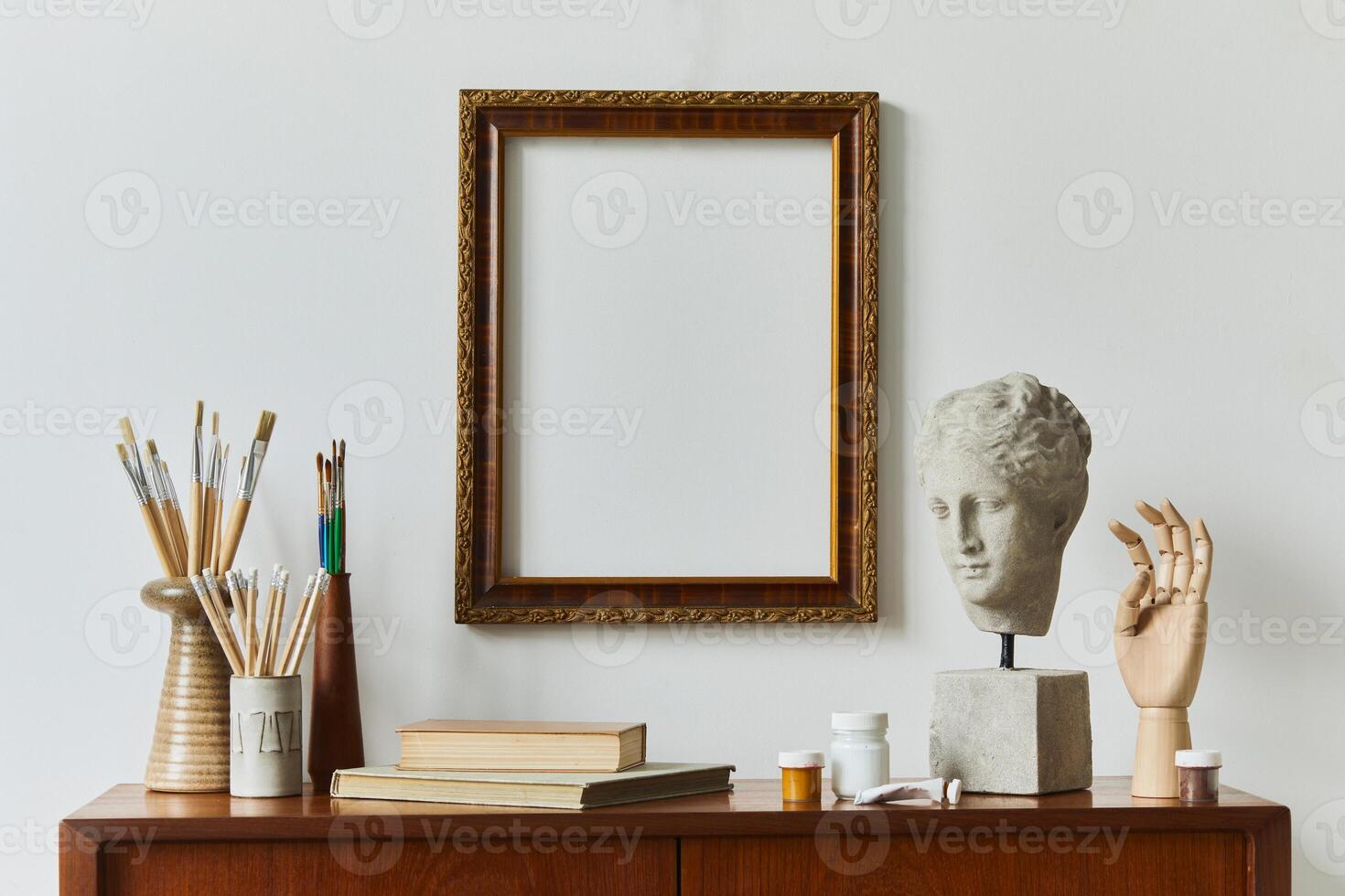 Stylish composition of artist workspace room with design retro teak commode, mock up poster frame, book, decoration and painting accessories. Template. photo