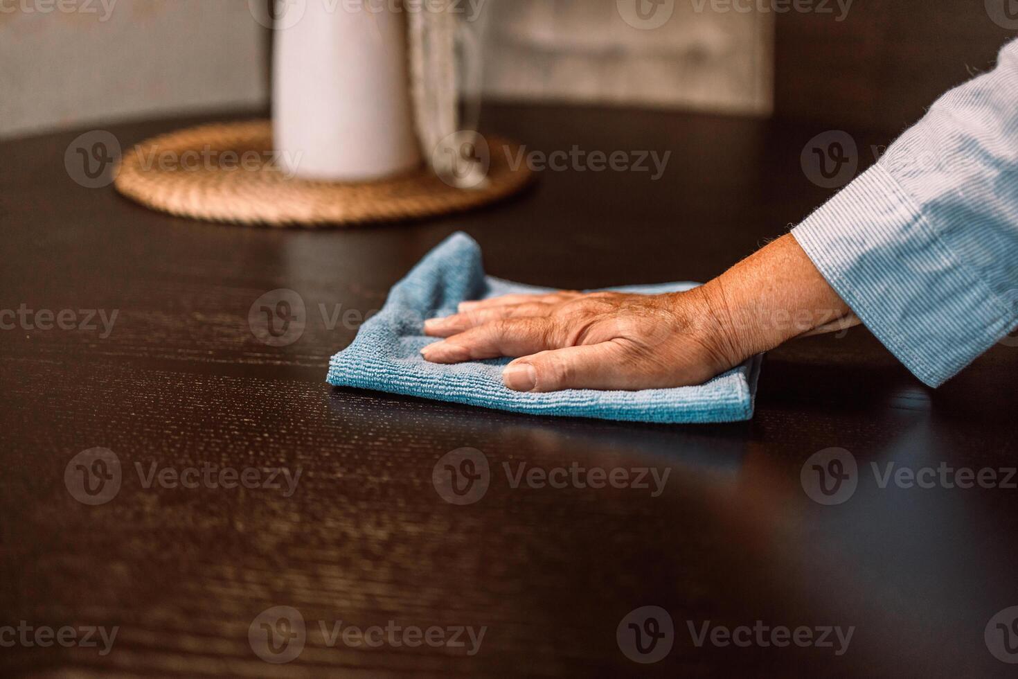 Close up woman cleaning wooden table using disinfectant blue towel. Prevent infection of Covid-19 virus, contamination of germs or bacteria, wipe or cleaning to eliminate, outbreak of Coronavirus. photo