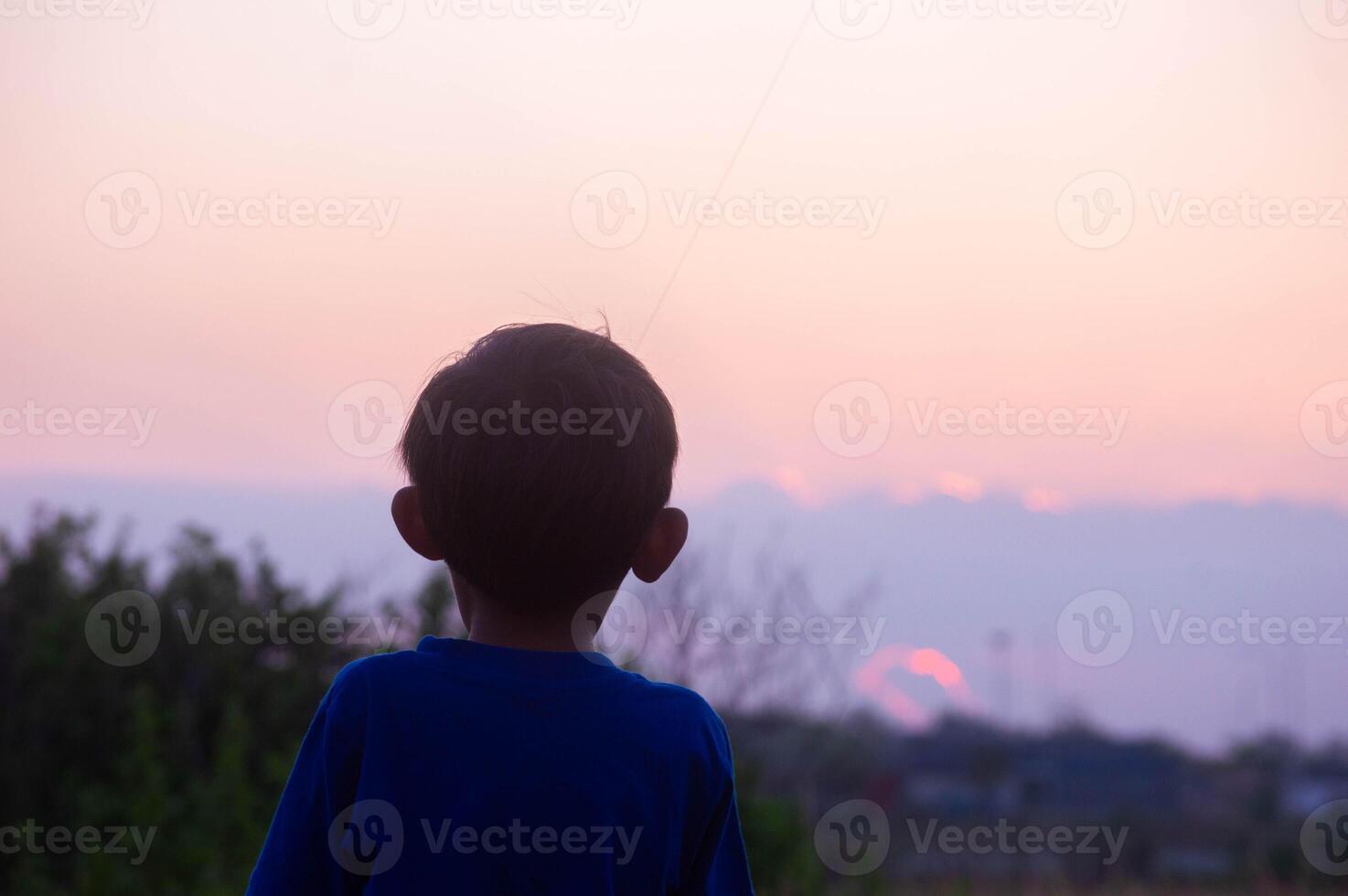 silhouette of a little boy in the field in the afternoon with orange sunlight photo