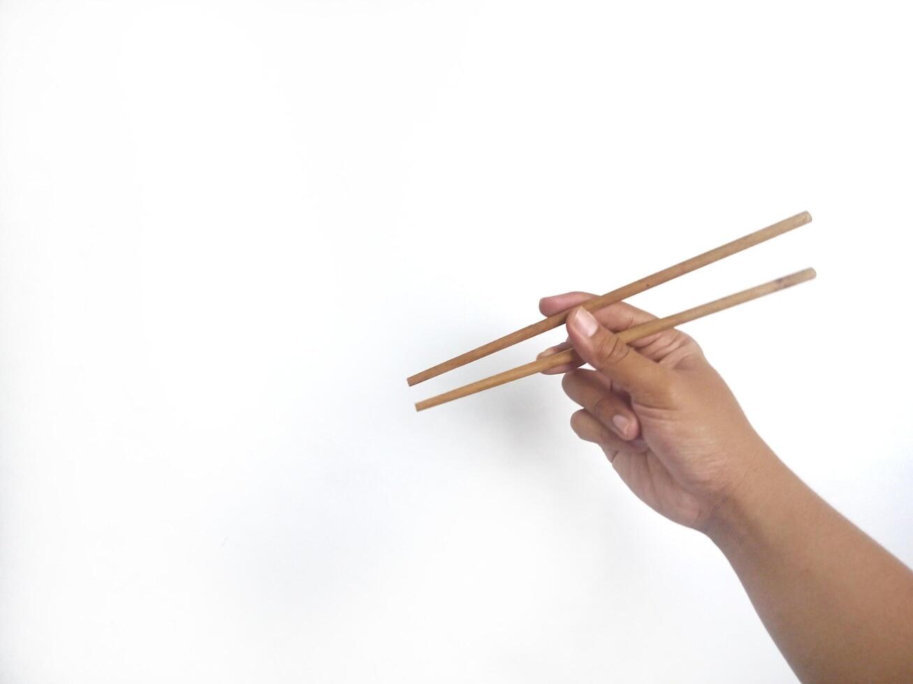 a hand holding a pair of wooden chopsticks against a plain white background. The focus is on the chopsticks, highlighting their smooth texture and natural wooden material. photo
