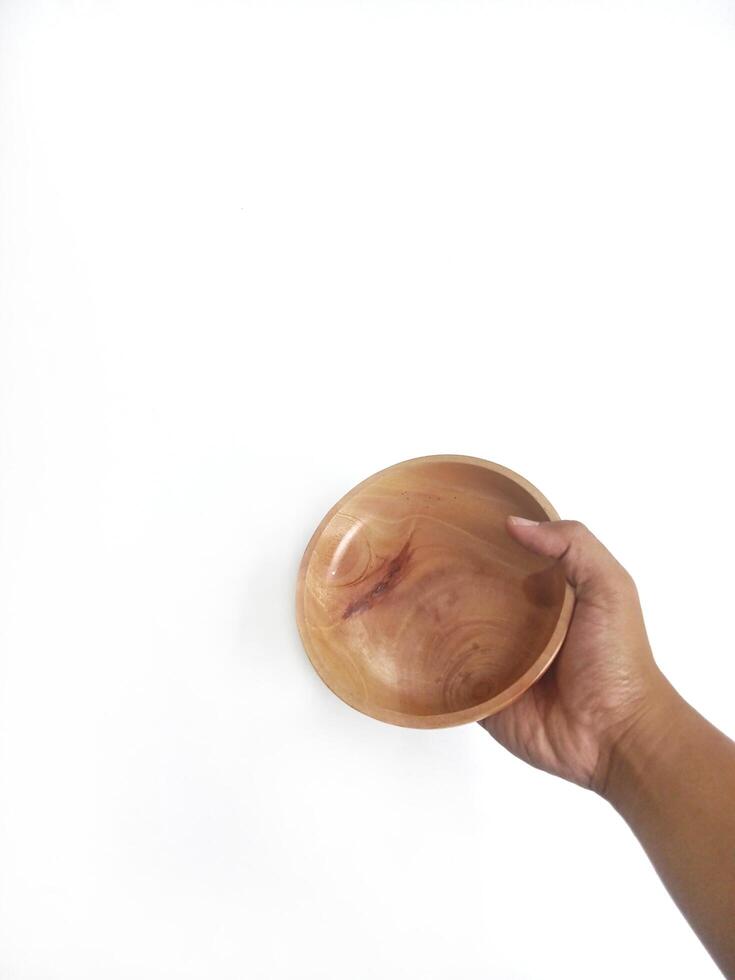 The image shows a hand holding a round wooden bowl with a smooth surface. The plain white background emphasizes the natural texture and grain patterns of the wood, making the bowl the central focus. photo