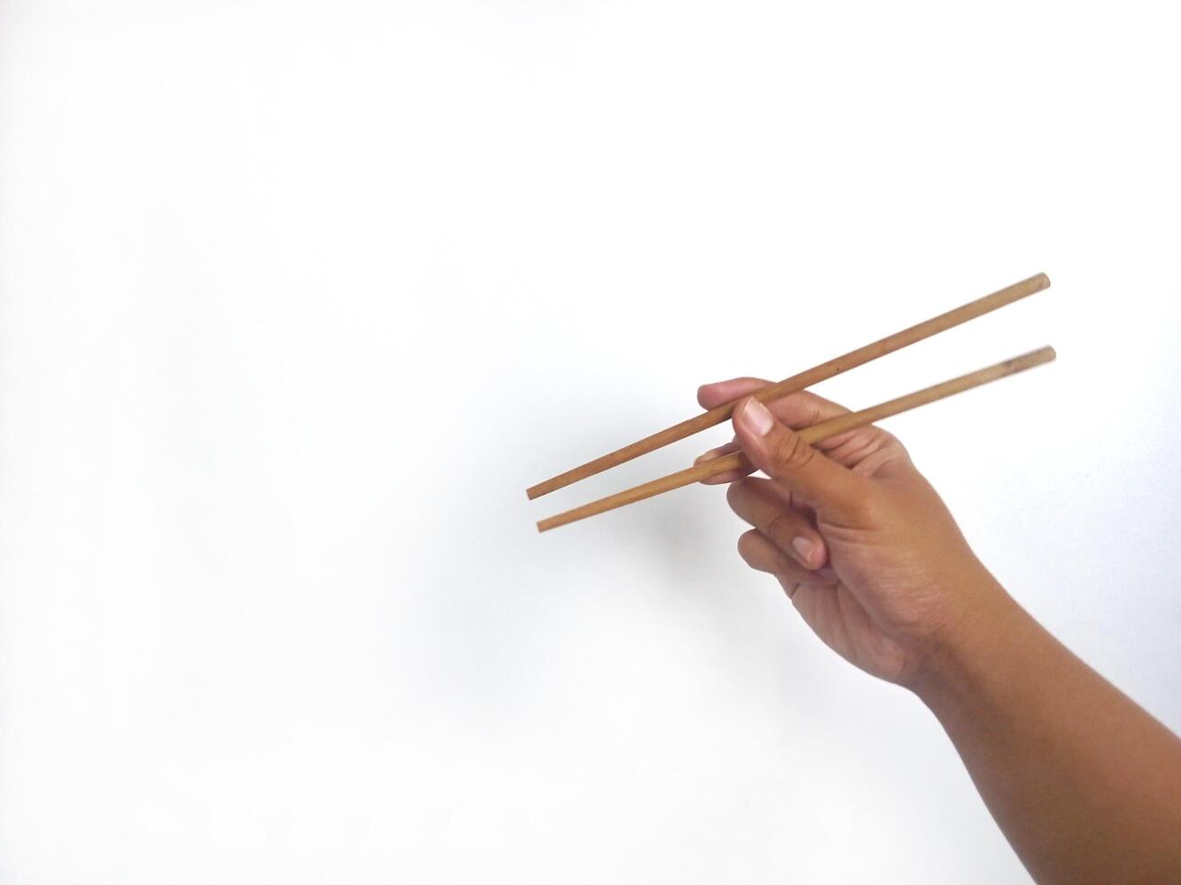 a hand holding a pair of wooden chopsticks against a plain white background. The focus is on the chopsticks, highlighting their smooth texture and natural wooden material. photo