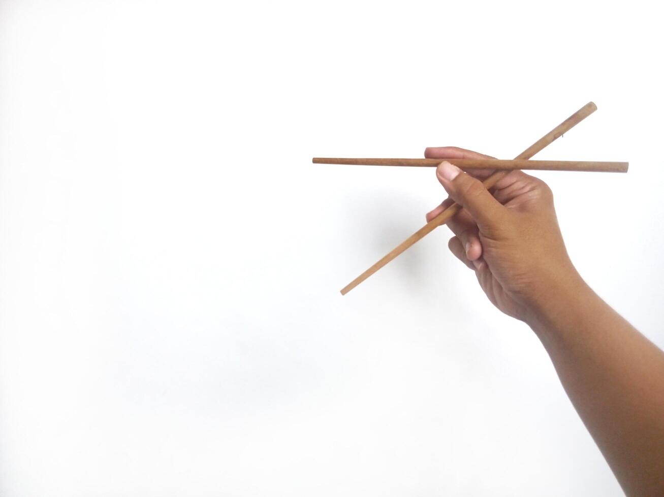 a hand holding a pair of wooden chopsticks against a plain white background. The focus is on the chopsticks, highlighting their smooth texture and natural wooden material. photo