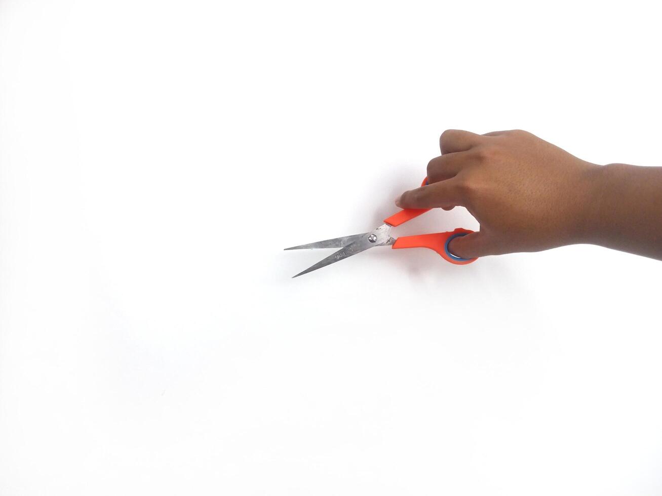 features a hand holding a pair of scissors with orange and blue handles. The scissors appear sharp and ready for use, set against a clean white background that draws attention to the main object. photo