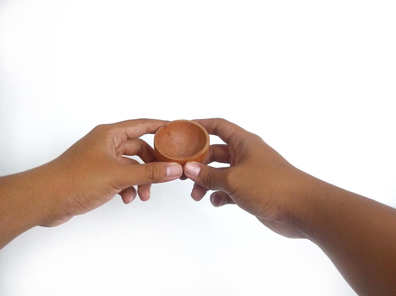 The image shows a pair of hands holding a little round wooden bowl with a smooth surface. The plain white background emphasizes the natural texture and grain patterns of the wood photo