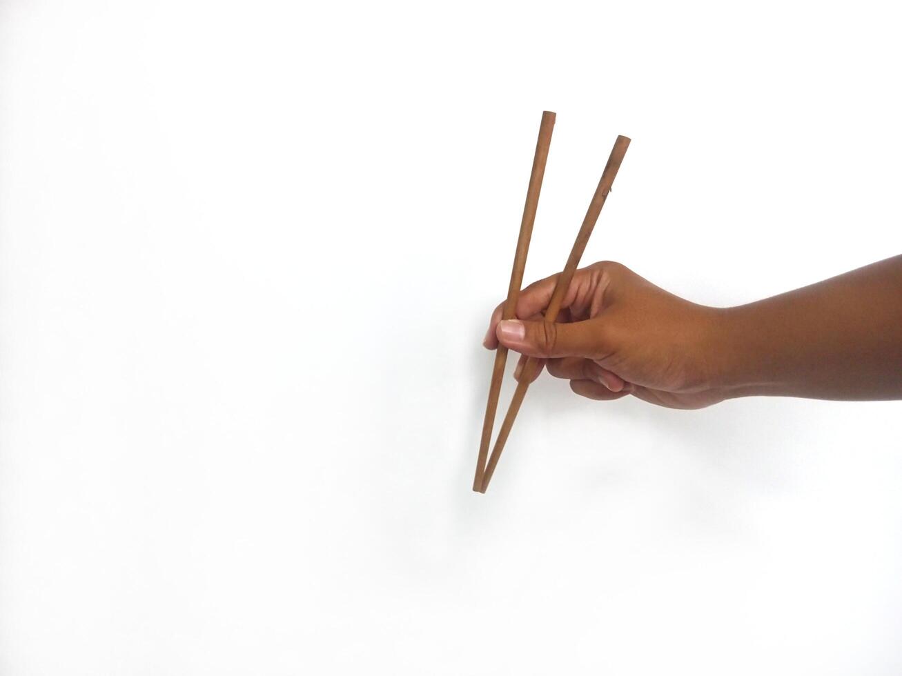 a hand holding a pair of wooden chopsticks against a plain white background. The focus is on the chopsticks, highlighting their smooth texture and natural wooden material. photo