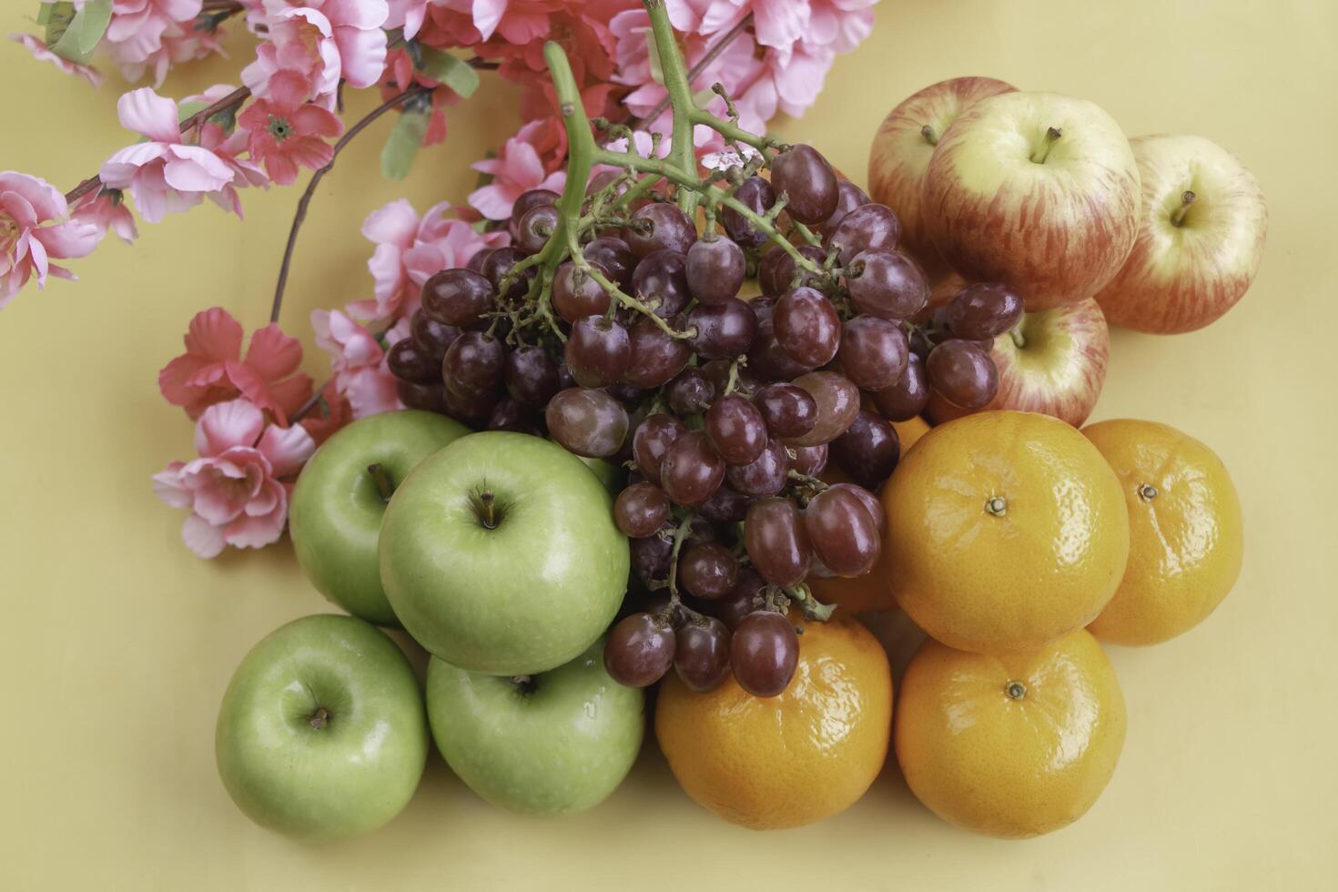 Grapes,Oranges and Apples put at the right side of blurred pink flowers, photo
