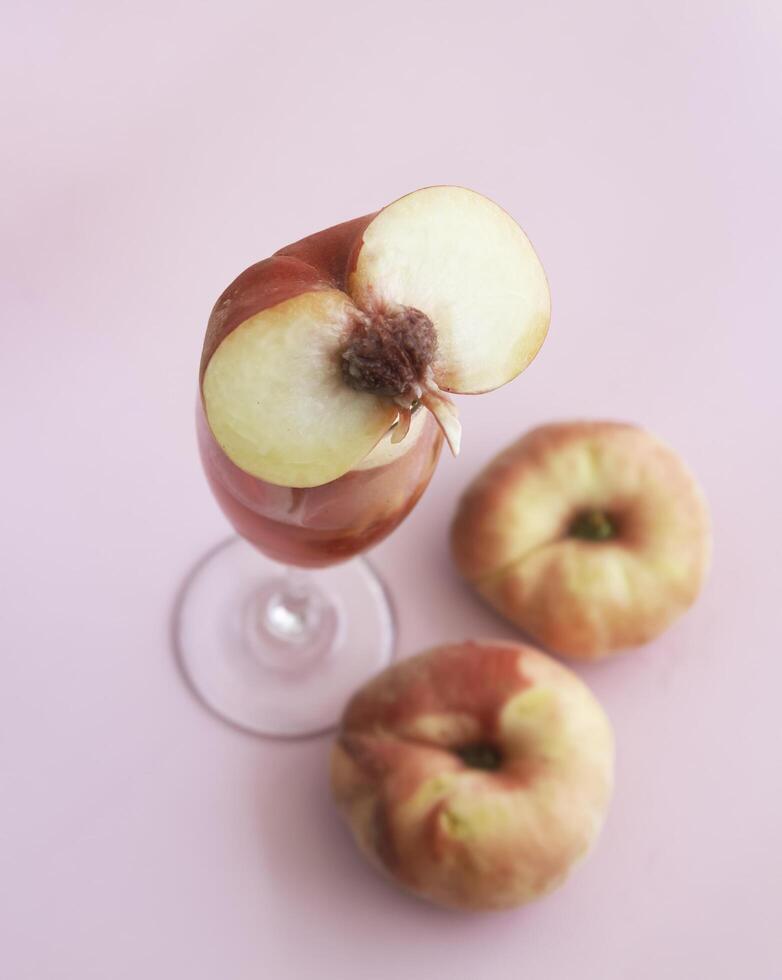 Cutted of Peach fruit with red peel put on blurred mouth of glass wine,on pink background, photo