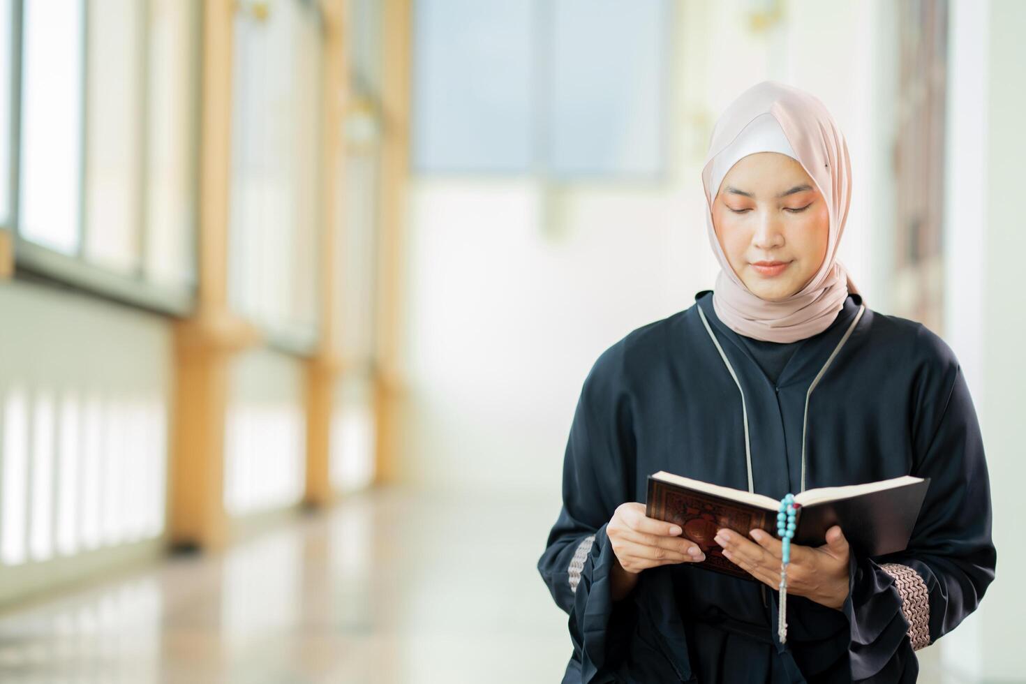 The image of an Asian Muslim woman in the Islamic religion in hijab in cream color. reading the Quran and having a happy smiling face Staying in a beautiful mosque out of respect for God. photo