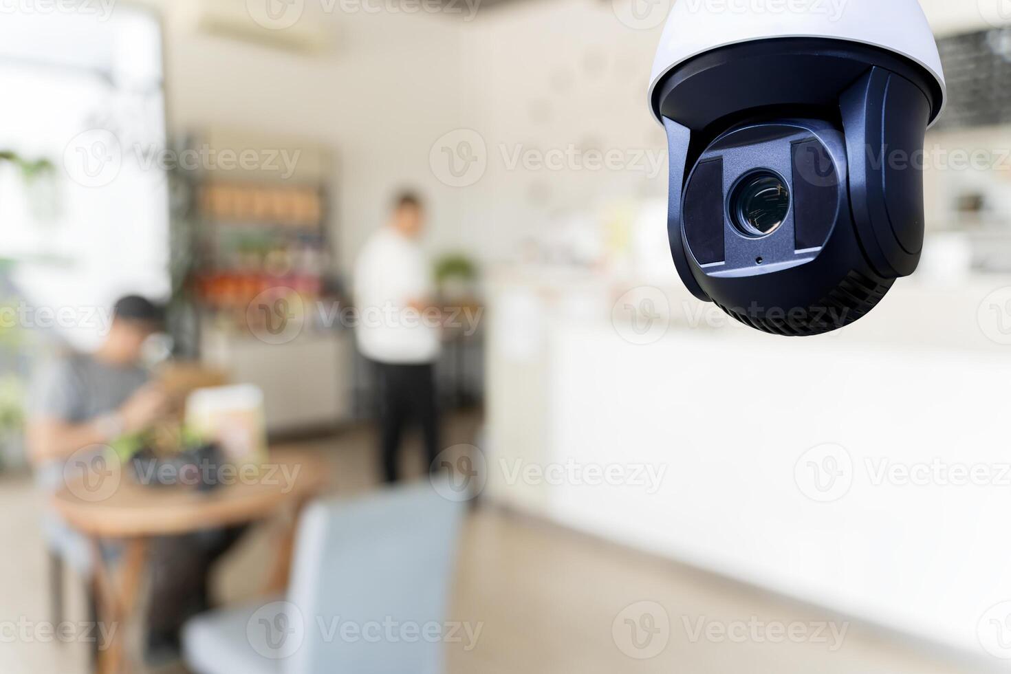 A security camera hangs from the ceiling of a cafe, with the interior of the cafe blurred in the background. photo