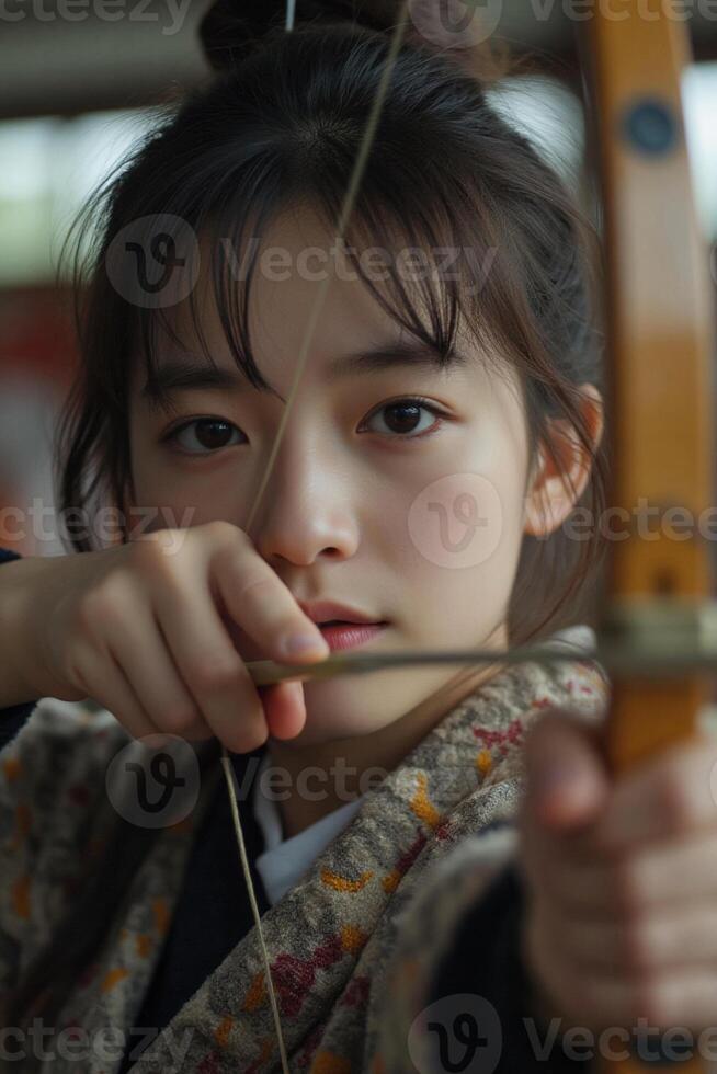 A Japanese teenage girl pulling back the bowstring during kyudo practice in her school s dojo photo