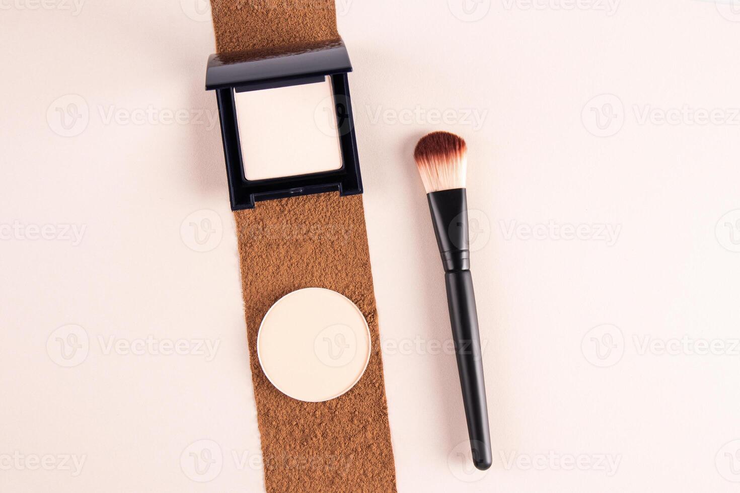 Compact powder in black packaging and round block refill in natural tone lie on the trail of loose powder in a dark tone. Makeup brush. top view photo