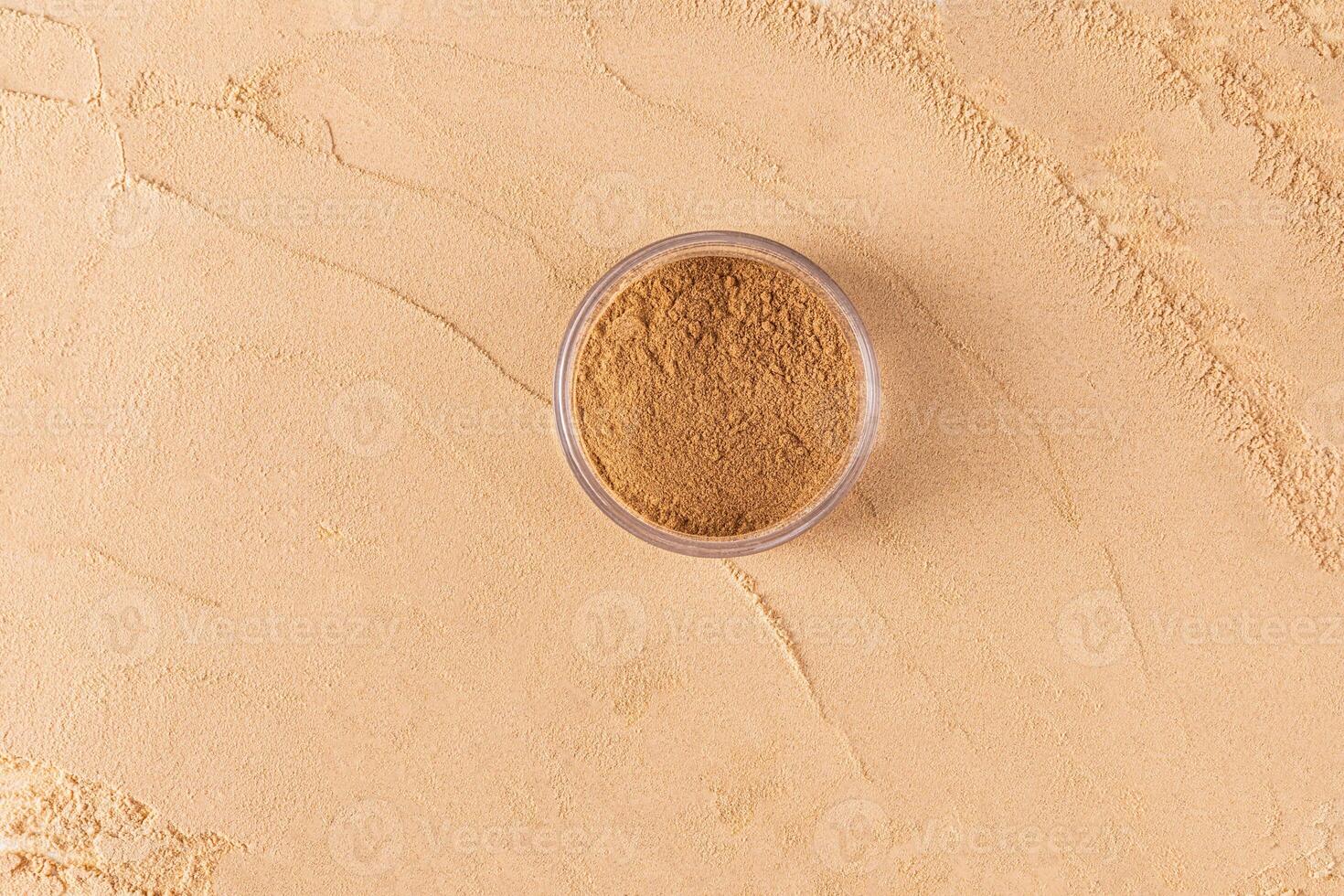 A round transparent jar with loose powder in bronze tone stands on a large sample of powder in a natural tone. top view. texture. A copy space. photo