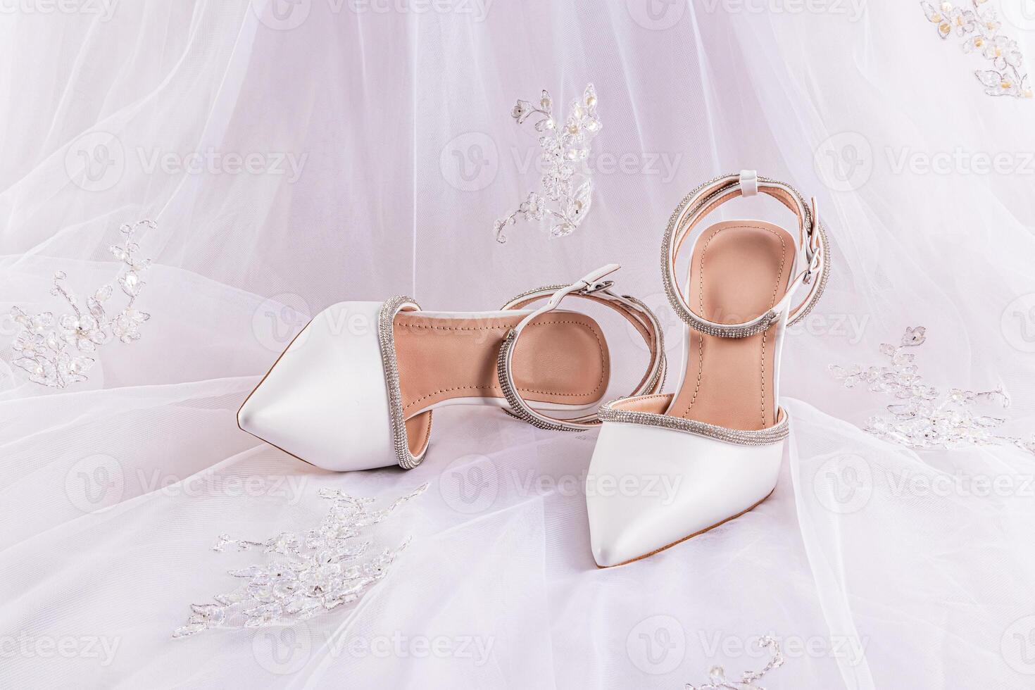 A pair of elegant bridal shoes on white satin with luxurious embroidery and a bridal veil. Front view. A copy space. The concept of the wedding. photo