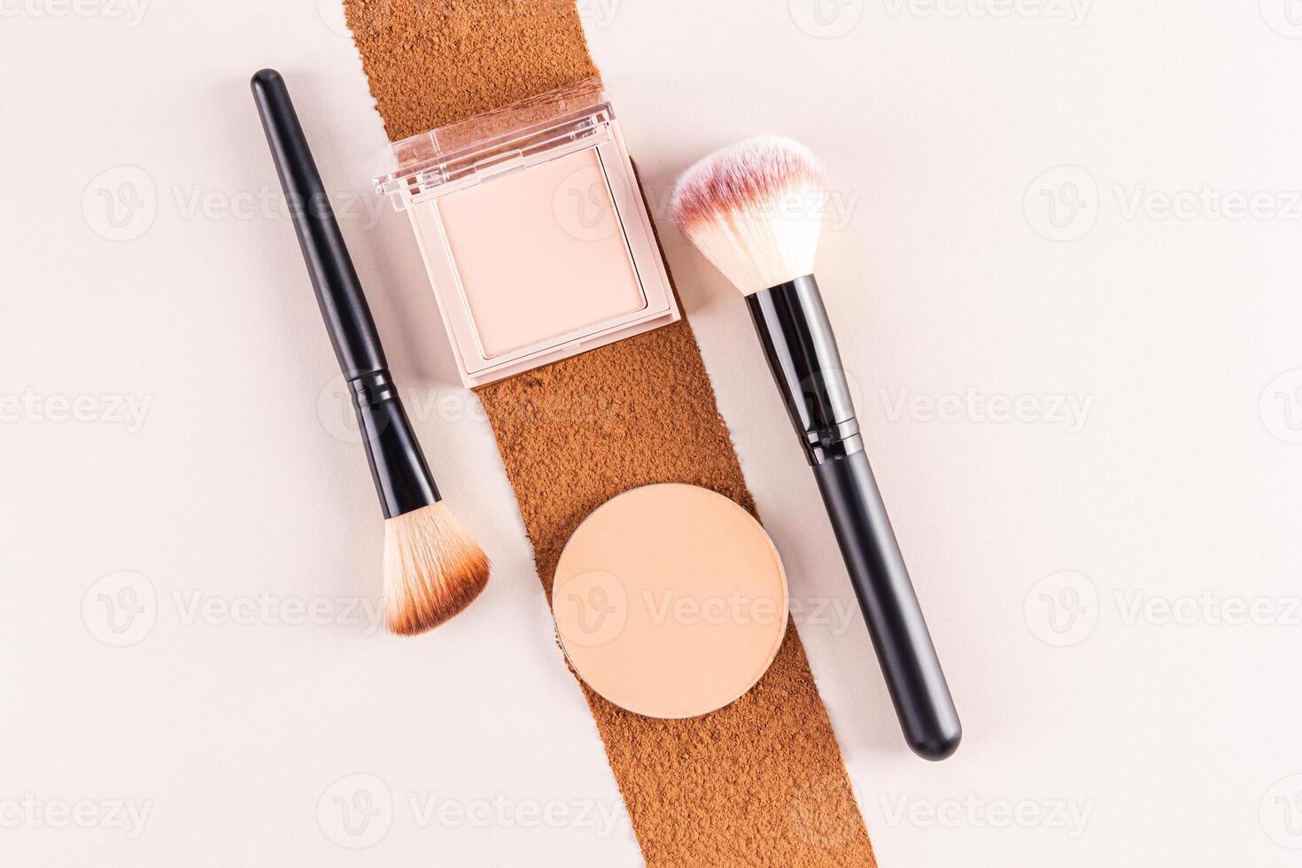 A pack of compact powder of a natural tone, a round block, a refill of a beige tone lie on a trace of dark dry powder. Two makeup brushes. top view. photo
