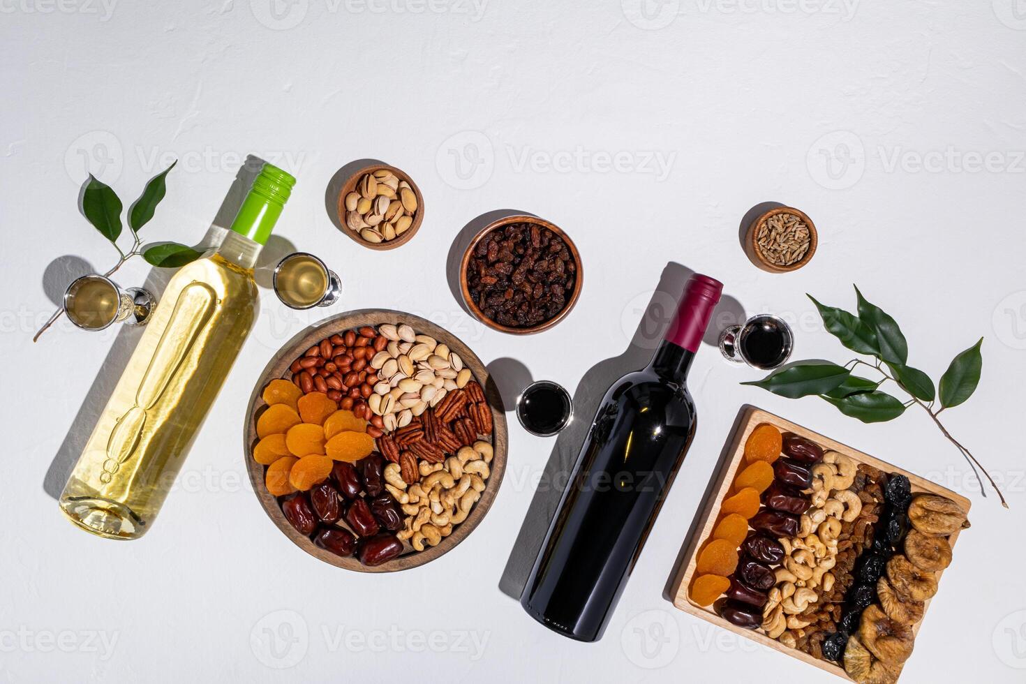 Two wooden trays with a mix of dried fruits and nuts, two bottles of red and white wine, glasses of wine, green tree branches. Tu be shvat. top view photo