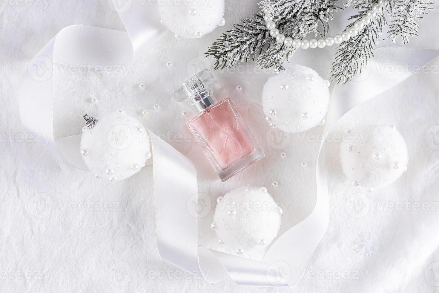 A beautiful bottle of pink perfume lies among the New Year's white balls on a mechanical background with a satin ribbon and a spruce branch. top view. photo