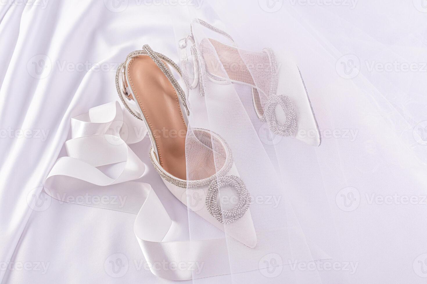 chic white bridal shoes on a white satin background with pleats under a delicate transparent veil. Festive still life. A copy space. photo