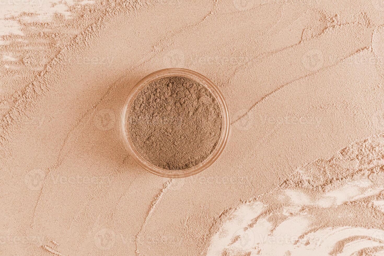 A transparent jar of loose powder in a dark tone stands on a large sample of powder. texture of decorative cosmetics. top view. A copy of the space. photo