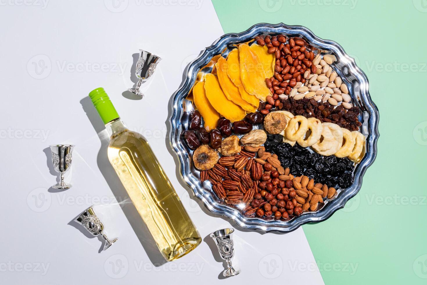 A large silver seder with traditional Tu be Shvat treats and a bottle of wine with silver glasses on a light background. top view. photo