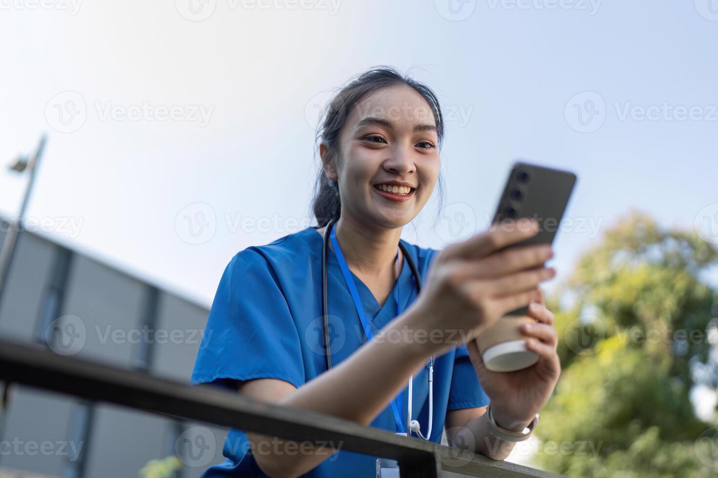 Young Asian Female Nurse Enjoying a Break Outdoors with Phone photo