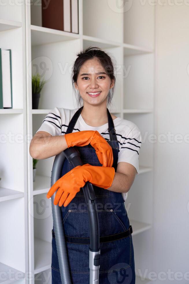 Radiant young Asian woman smiling while holding a vacuum cleaner, ready to clean. photo