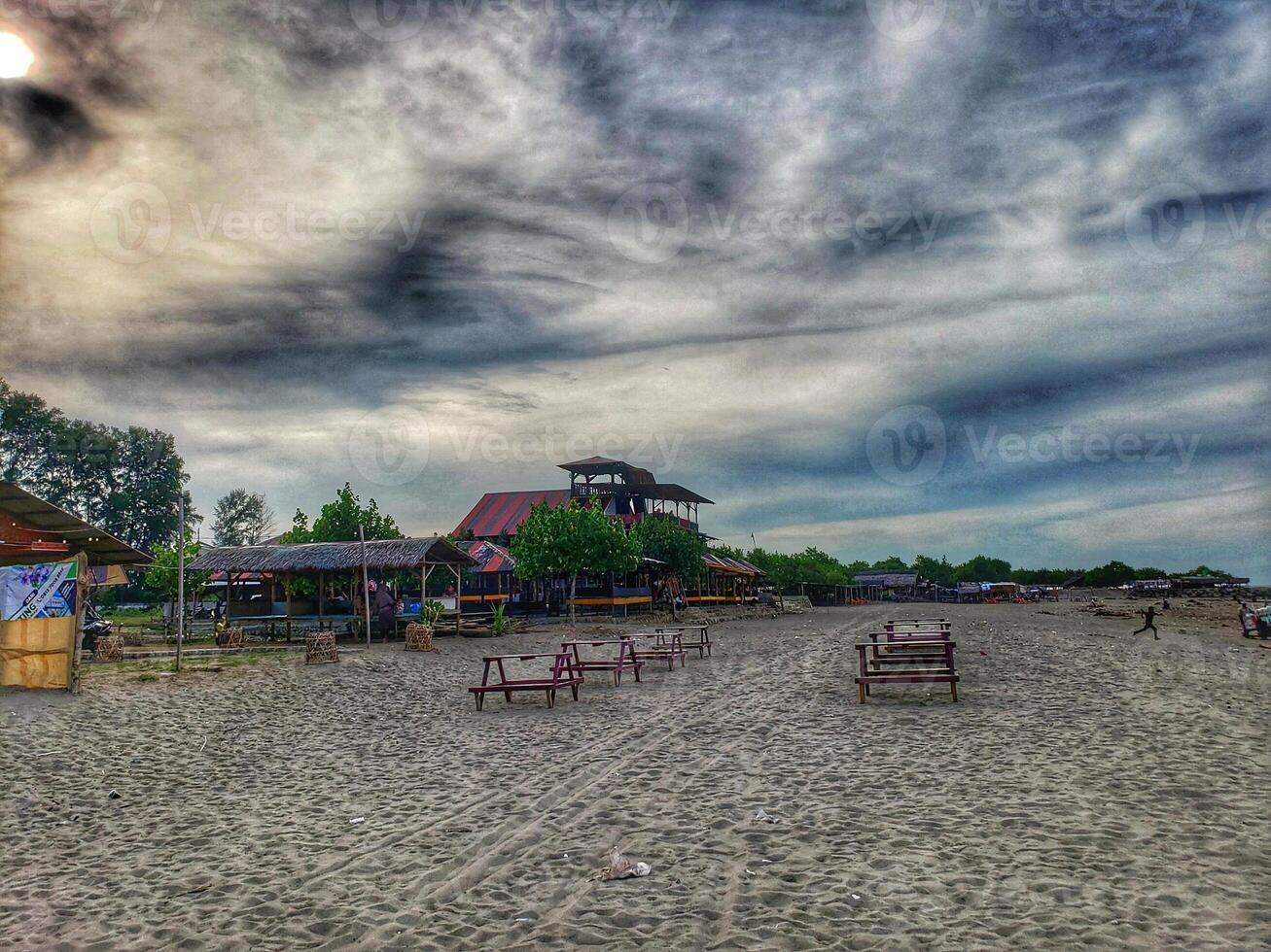 A beach with benches and a building under a cloudy sky photo
