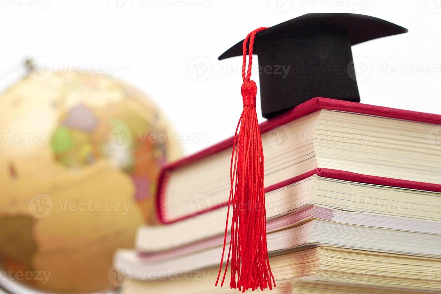 A Graduation cap placed on a stack of books and blurred globe behind. It is the concept of education, knowledge, learning and successful. photo
