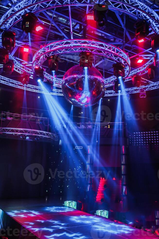 night disco club with neon blue violet red light, disco mirror ball and bright floodlight with round metal frame luminous construction photo