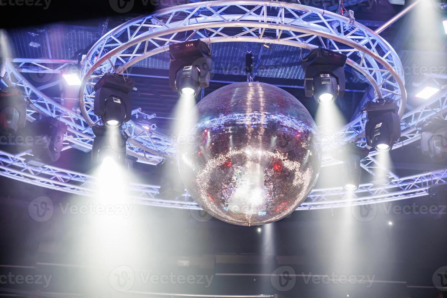 night disco club with neon blue violet red light, disco mirror ball and bright floodlight with round metal frame luminous construction photo