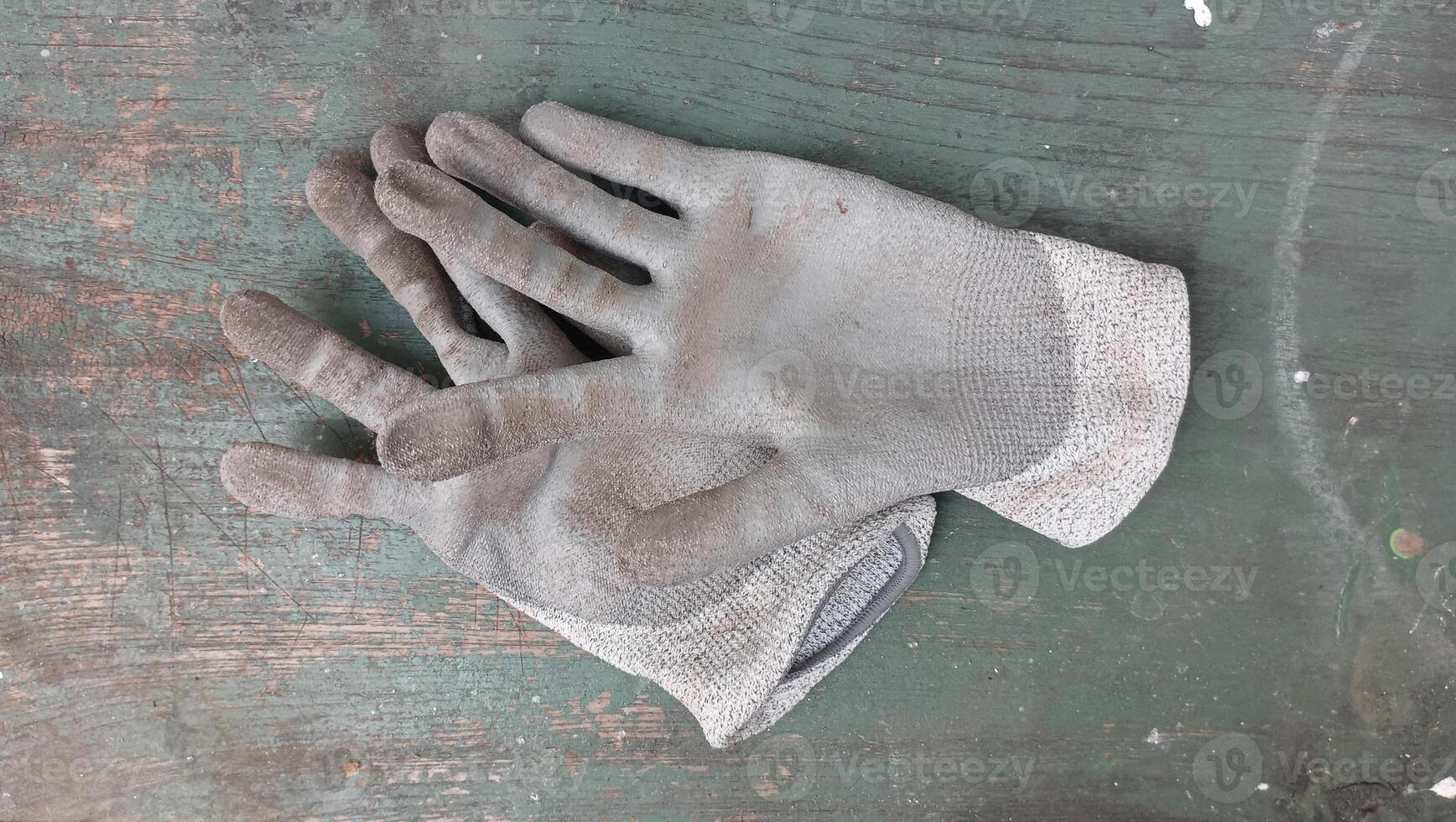 A pair of old work gloves laying on a green surface photo