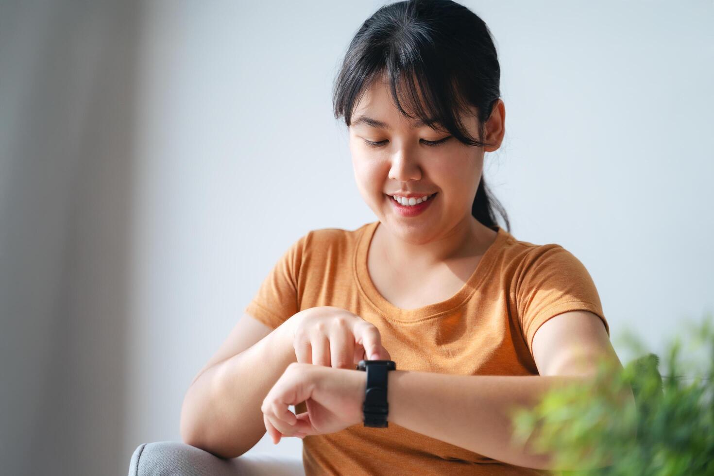 Happy young woman is using smartwatch on her wrist to check health data, notifications, set alarm. photo