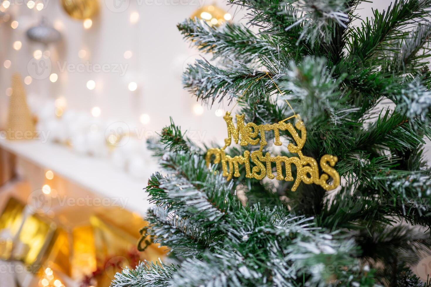 A close-up of a merry christmas text toy on a Christmas tree with lights on background. High quality photo