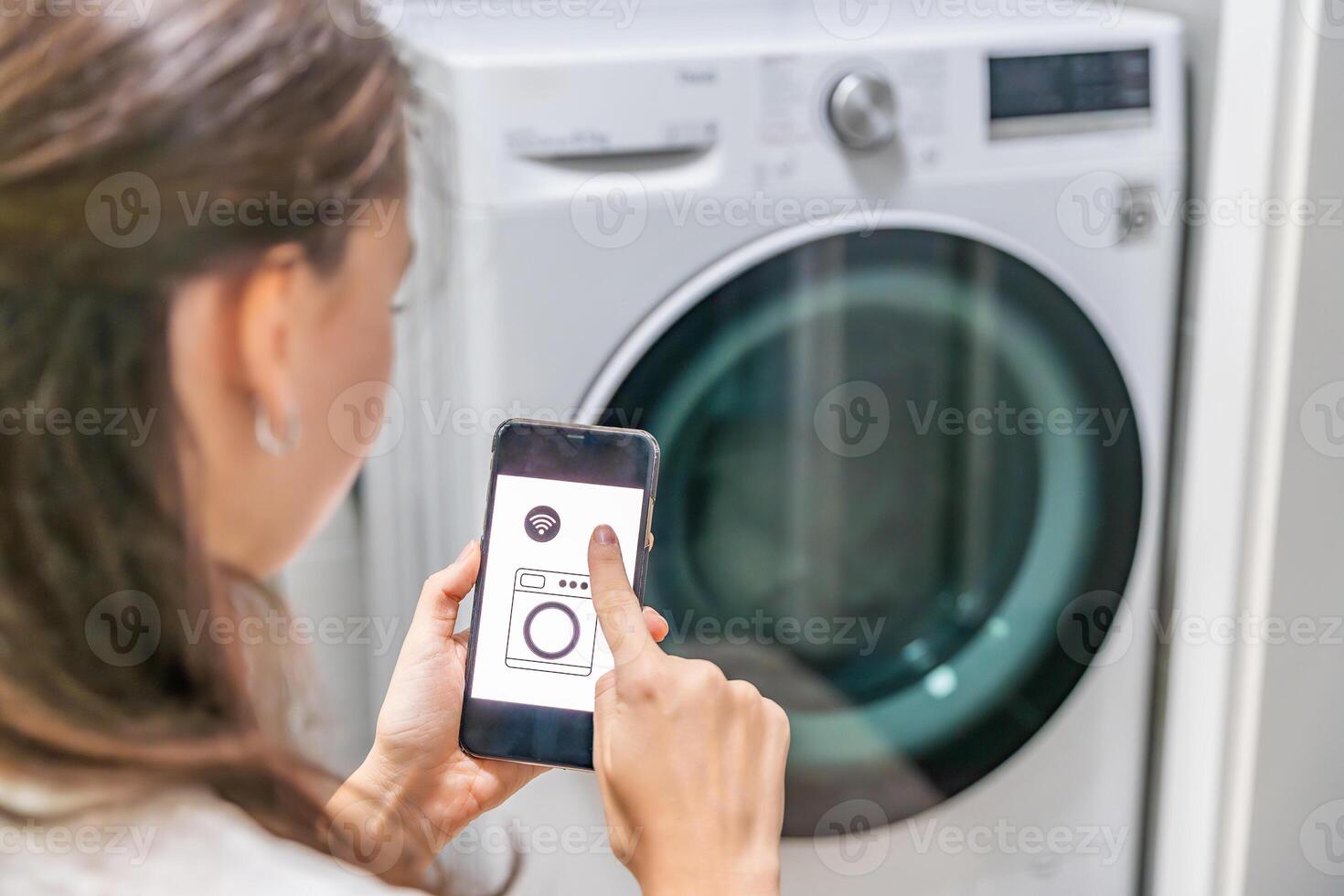 Young woman using mobile phone control via wi-fi and app for washing machine in home. Homesmart and new technology concept. High quality photo