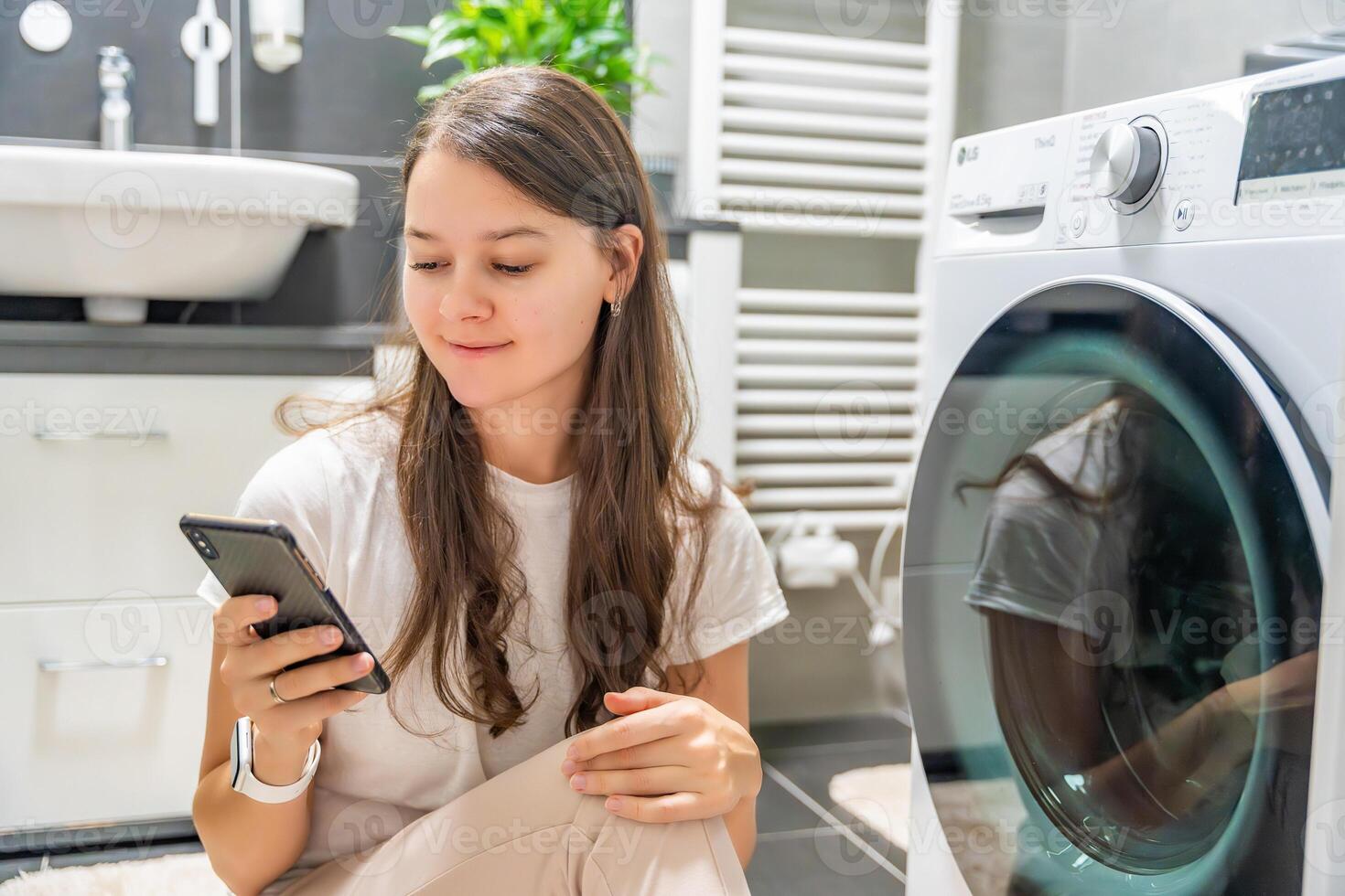 Young woman using mobile phone control via wi-fi and app for washing machine in home. Homesmart and new technology concept. High quality photo