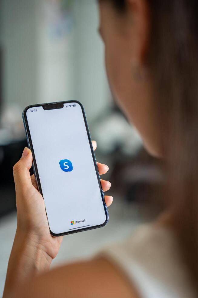 Prague, Czech republic - May 2, 2024. Woman holding iPhone with logo of application Skype on the screen, using mobile application for business home. High quality photo