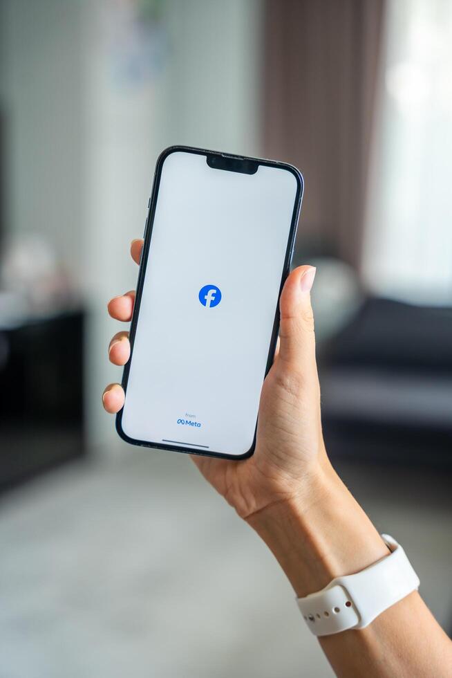 Prague, Czech republic - May 2, 2024. Woman holding iPhone with logo of application Meta Facebook on the screen, using mobile application for business home. High quality photo
