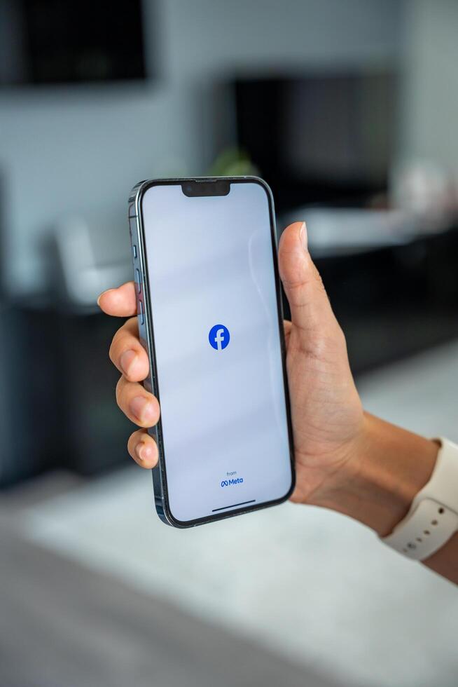 Prague, Czech republic - May 2, 2024. Woman holding iPhone with logo of application Meta Facebook on the screen, using mobile application for business home. High quality photo