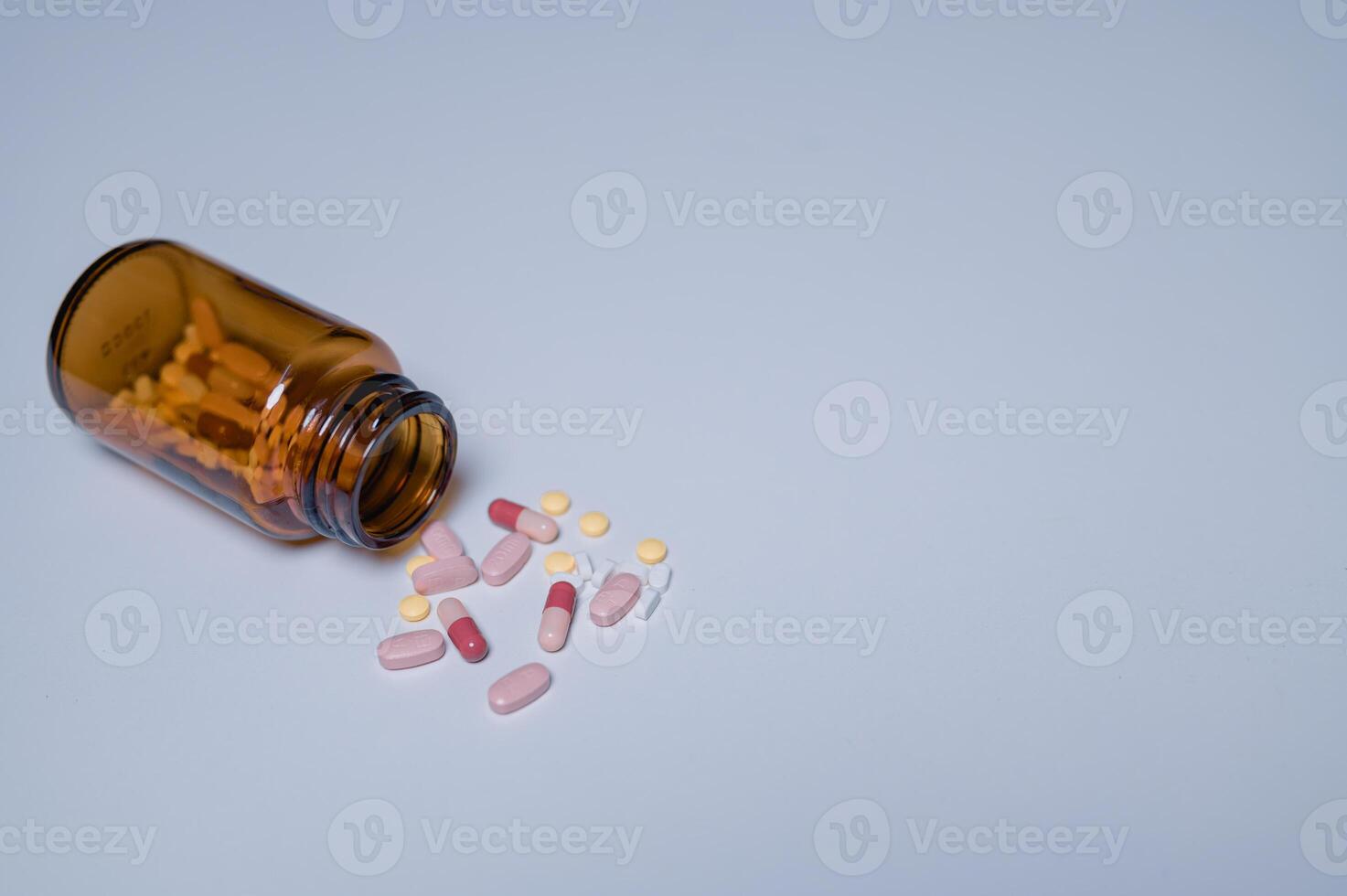 Spilled amber pill bottle various colorful tablets and capsules scattered on plain background, highlighting importance of careful medication storage and handling photo