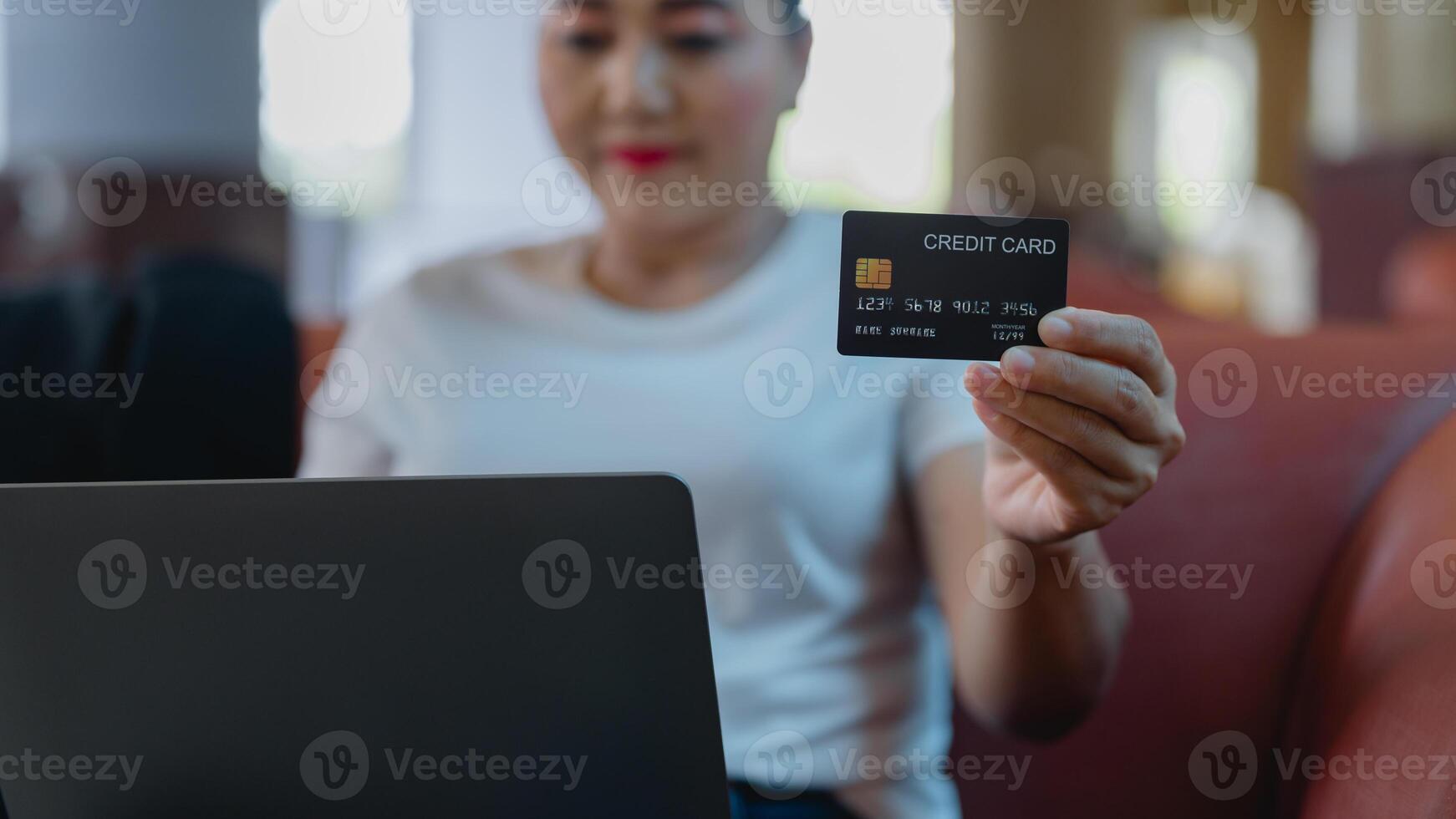 Woman holds credit card in one hand while working on laptop, convenience of online shopping and digital payments in relaxed setting photo