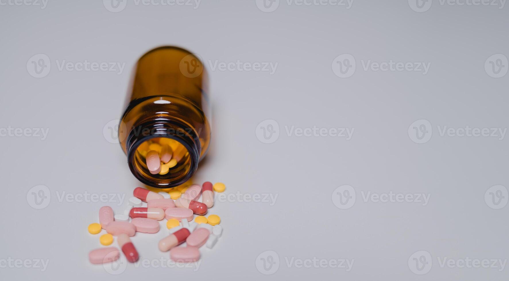 Close-up view of brown bottle tipped over, spilling colorful pills and capsules onto smooth surface, highlighting importance of medication safety and awareness photo