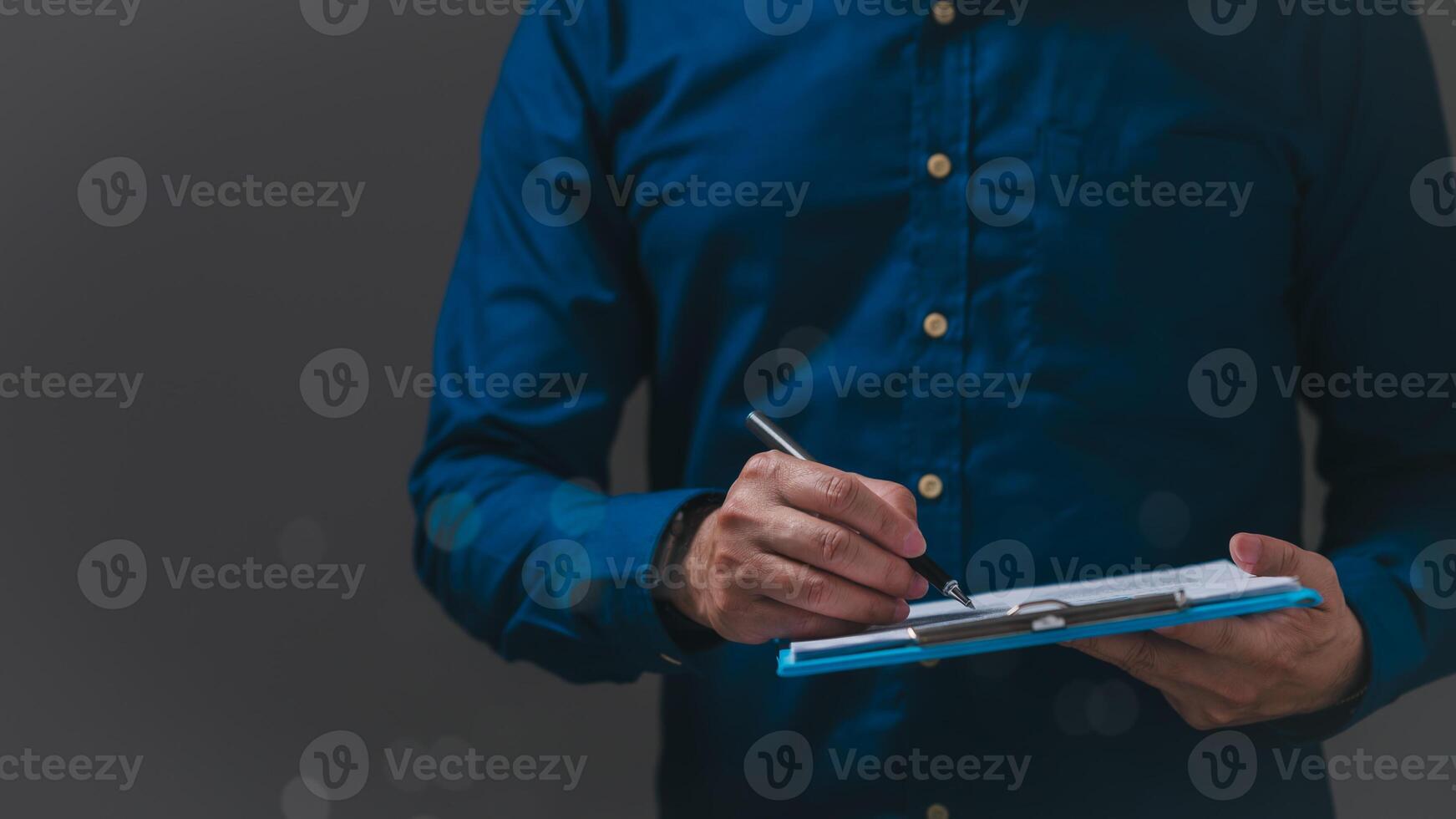 Person in blue shirt is diligently writing on clipboard, concentration and preparation in professional setting moment captures essence of effective communication photo