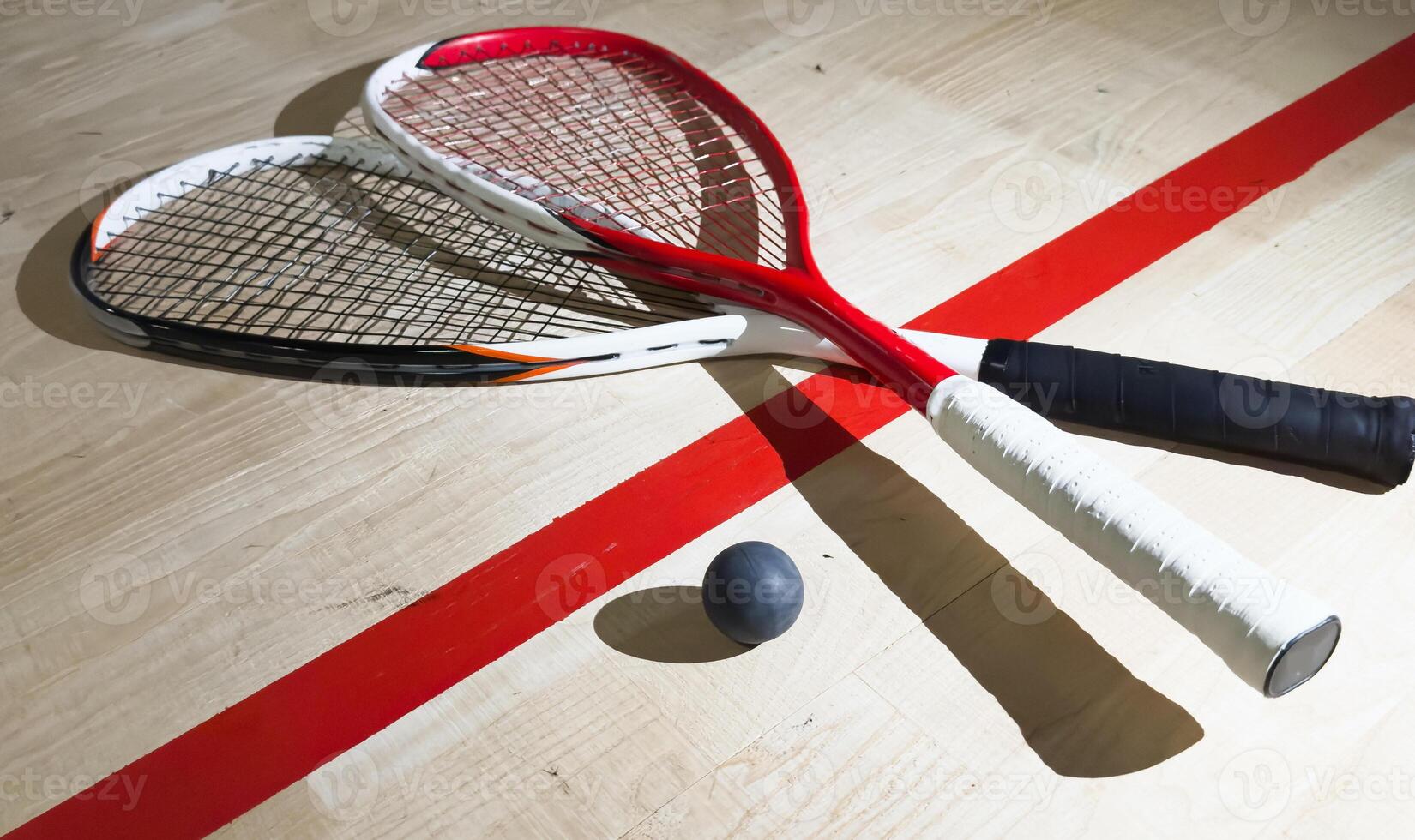 Two rackets and two squash balls lie on the parquet floor. Horizontal photo
