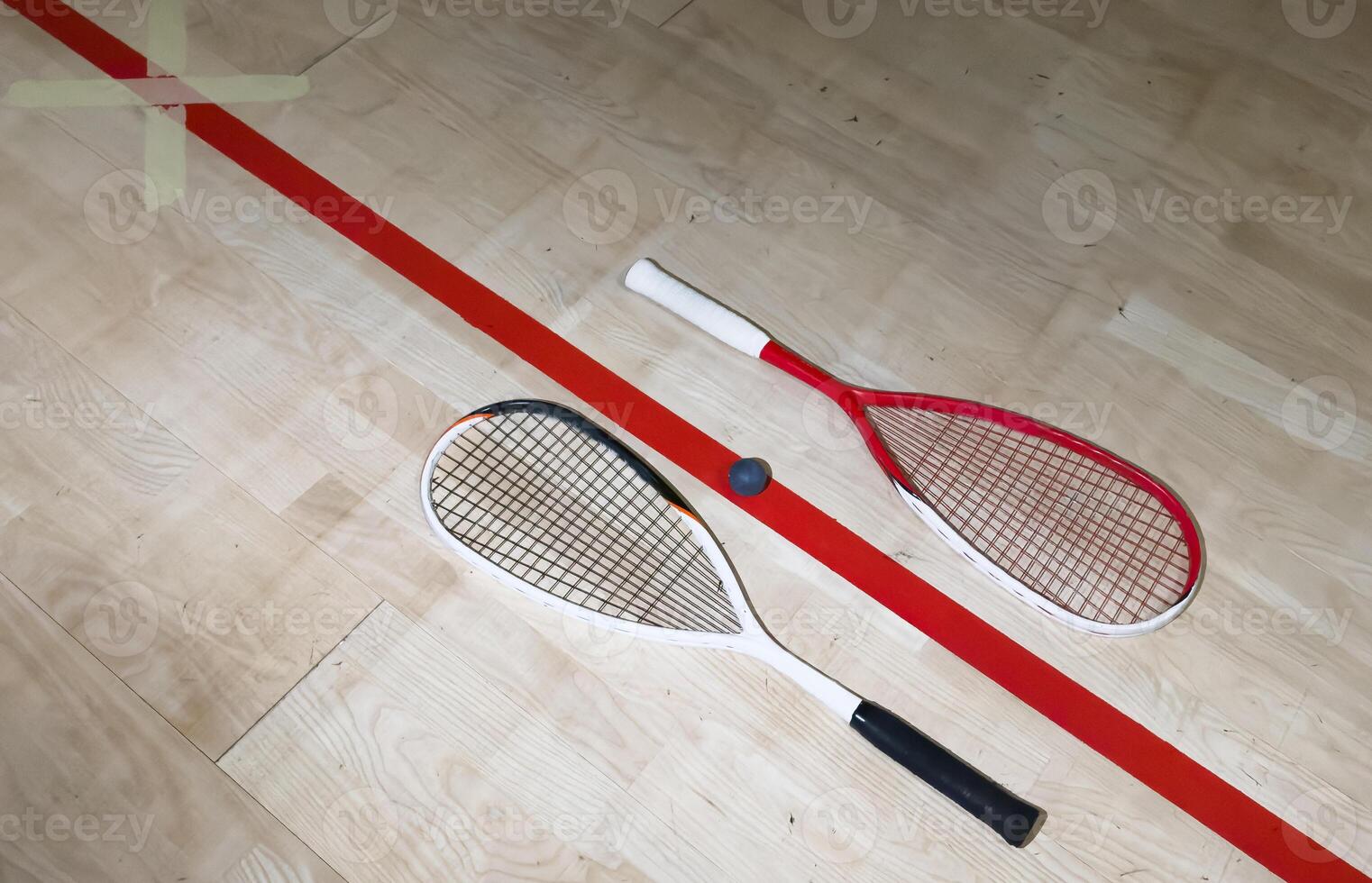Two rackets and two squash balls lie on the parquet floor. Horizontal photo